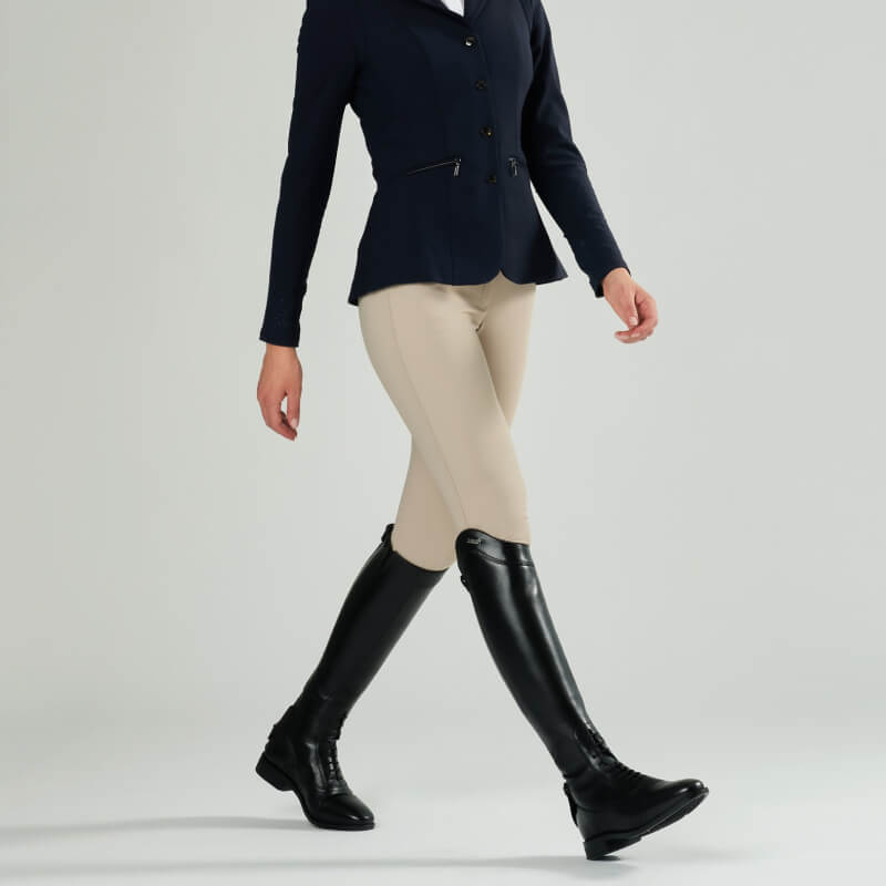 Person in beige breeches, navy jacket, and LeMieux Field Riding Boot Black Regular/Regular walking.