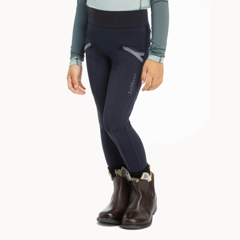 Child wears LeMieux Mini Pull Ons Navy breeches, long-sleeve top, and brown boots.