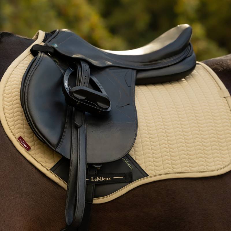 A black saddle on a LeMieux Essence Close Contact Square Pear pad rests on a horse outdoors.