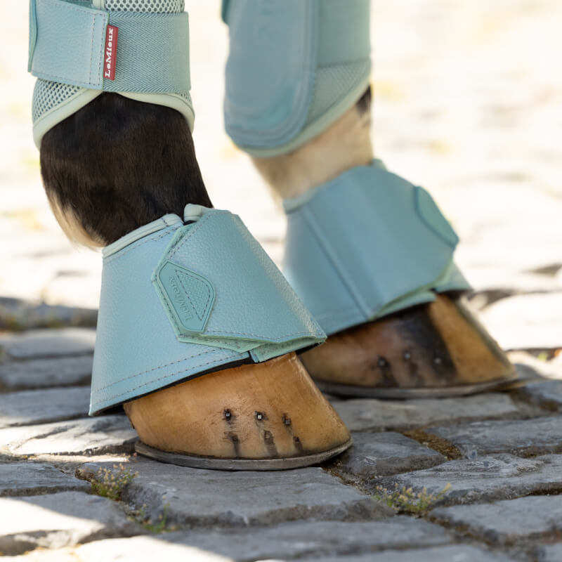 Close-up of a horse’s hooves in LeMieux Arika Over Reach Boots Aqua on cobblestone pavement.
