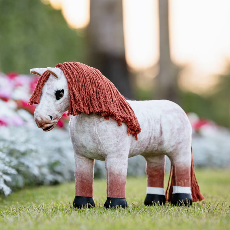 LeMieux Toy Pony Poppy, by LeMieux, with a brown mane stands on grass outdoors.