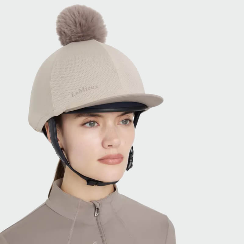 Woman wears LeMieux Maria Mesh Hat Silk Almond helmet cover with pom-pom and matching top.