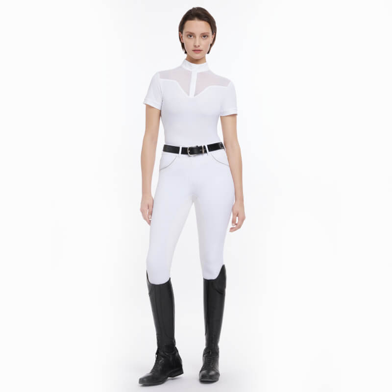 Person in a fitted LeMieux Emily SS Show Shirt White with black belt and tall black riding boots.