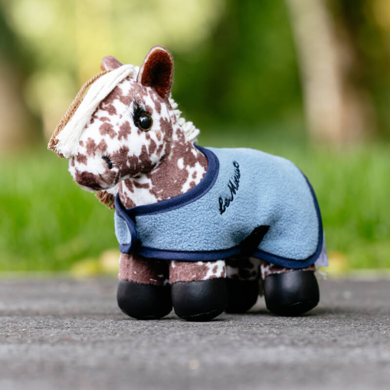 LeMieux Tiny Pony Montana plush toy stands outdoors wrapped in a blue blanket.