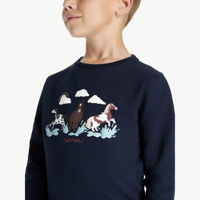 Child wears LeMieux Mini Poppy Long Sleeve Top Navy with horse, grass, and cloud design.