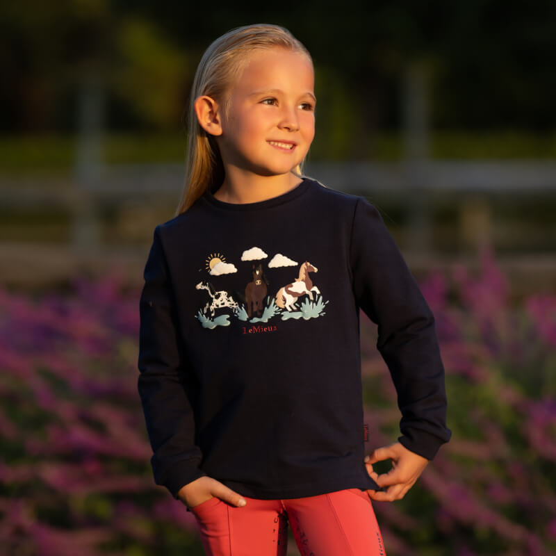 Girl in a LeMieux Mini Poppy Long Sleeve Top Navy and pink riding leggings outdoors.