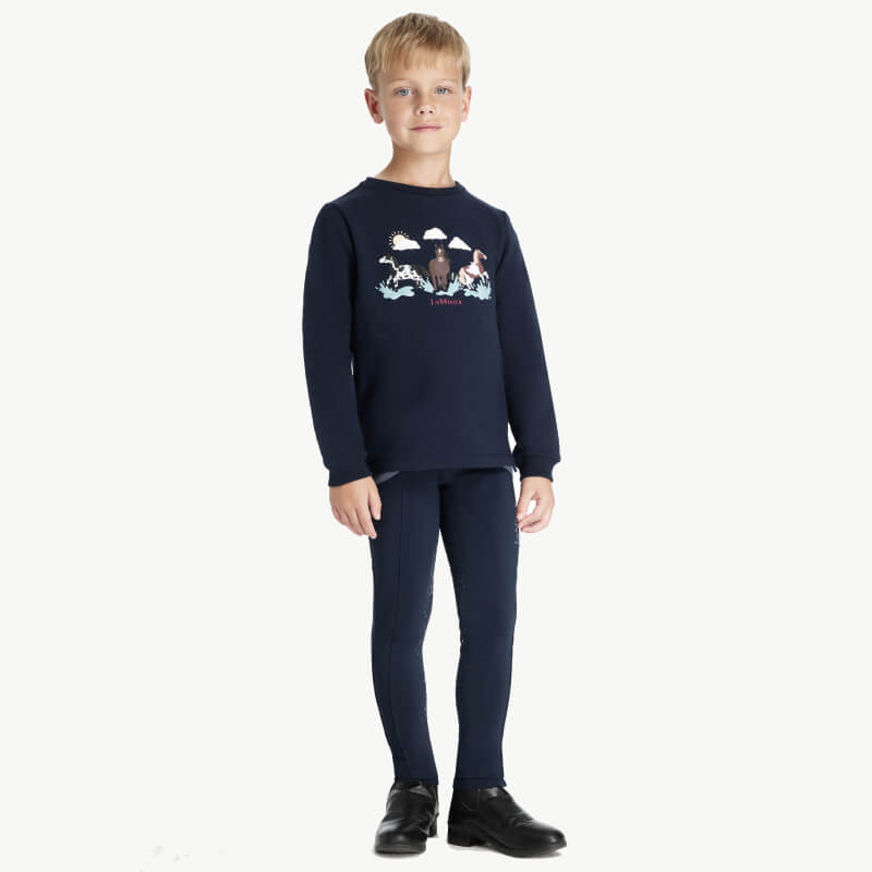 Young boy in a LeMieux Mini Poppy Long Sleeve Top Navy, smiling against a white background.