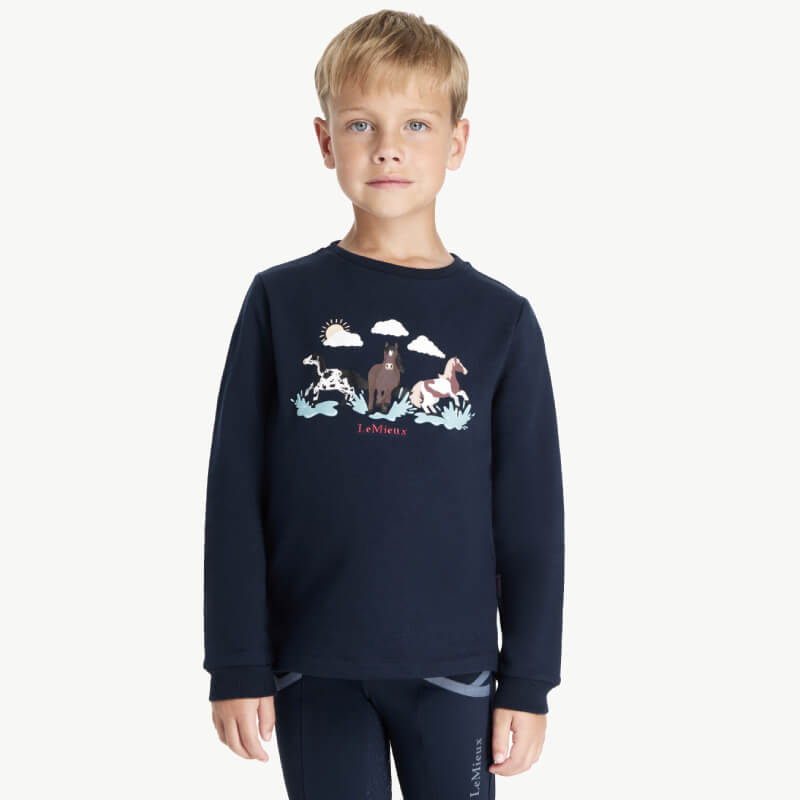 Young boy in a LeMieux Mini Poppy Long Sleeve Top Navy with horse and clouds graphic.