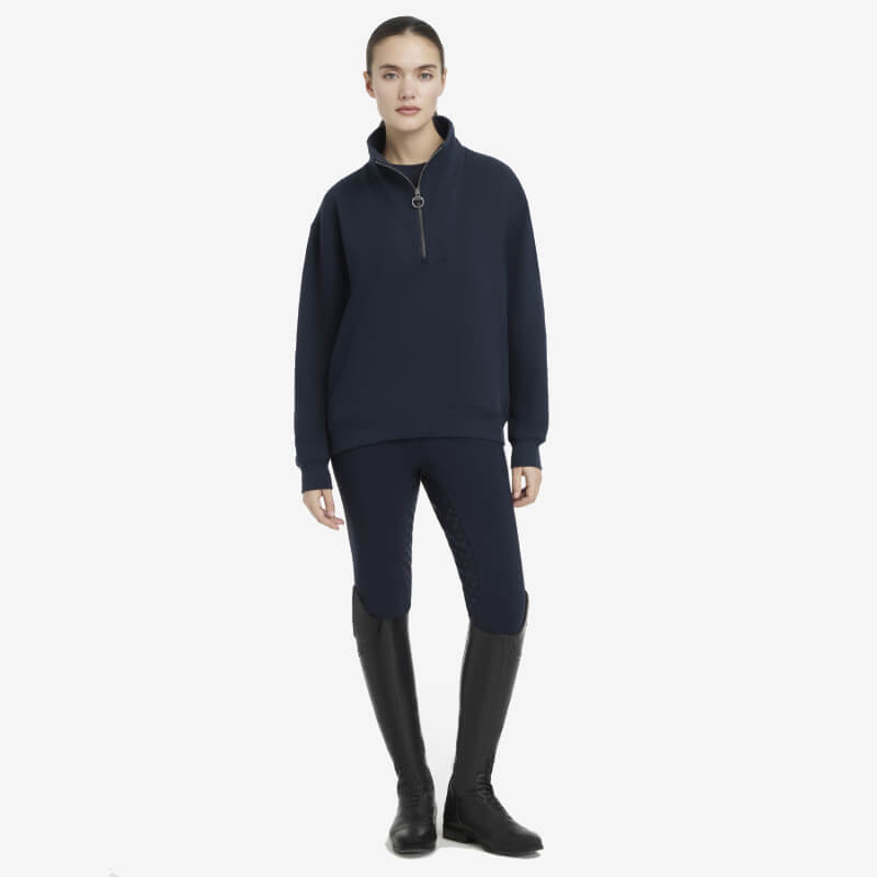 Woman in LeMieux Keira Quarter Neck Sweat Navy, matching pants, and tall black boots.