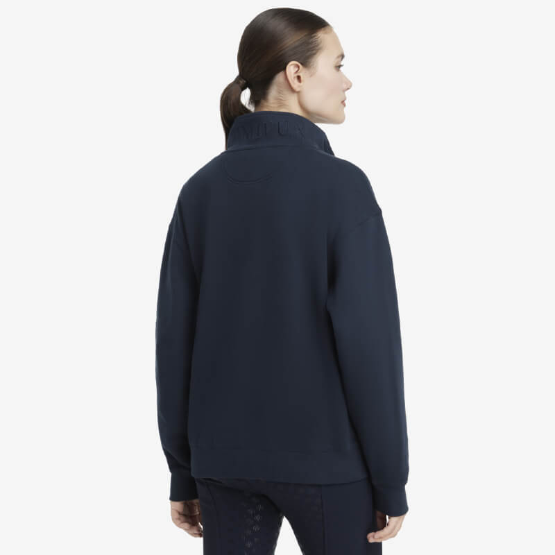 Woman in a LeMieux Keira Quarter Neck Sweat Navy, hair in low ponytail, plain background.