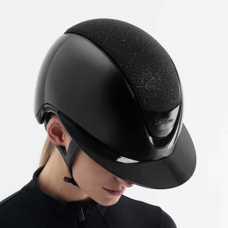 Woman wearing LeMieux Verv® Magnetic Top Panel helmet in Brilliance Black, looking downward.