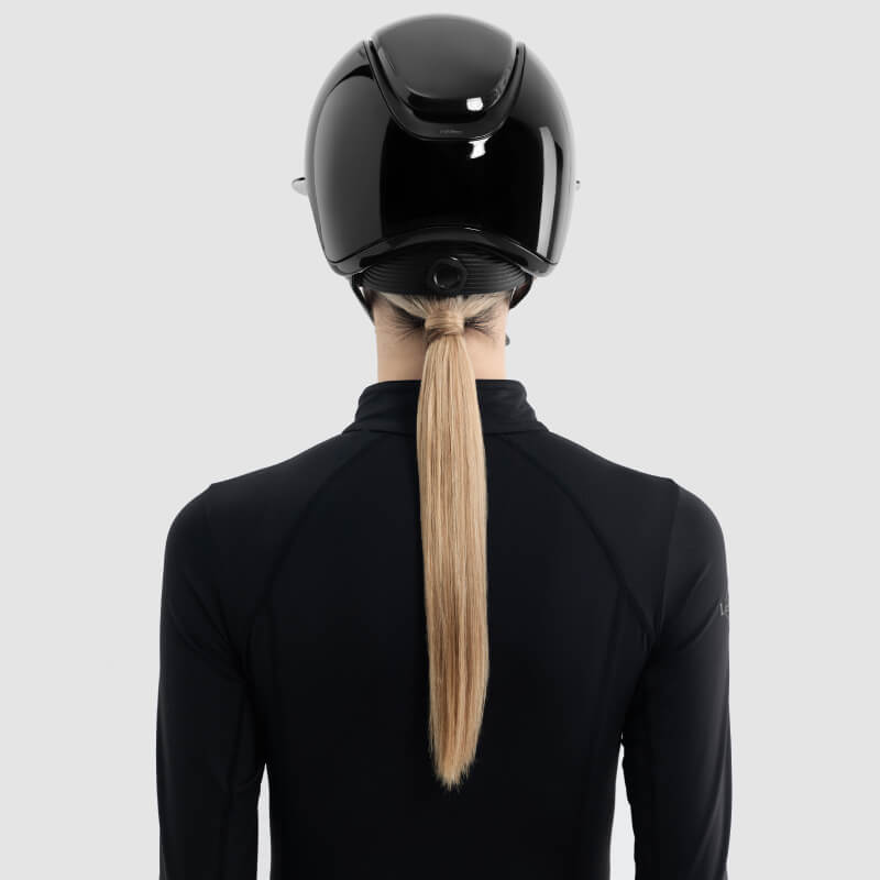 Person with long blonde ponytail wears LeMieux Verv® Gloss Black Competition Helmet, seen from behind.