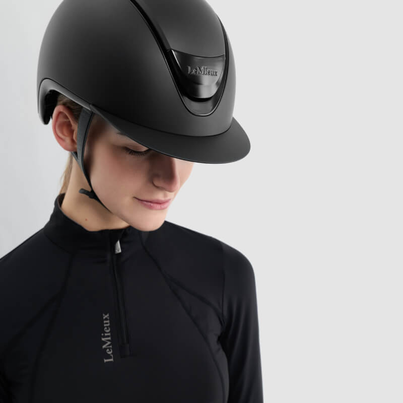 Woman wears LeMieux Verv® Competition Helmet Matte Black against a plain light background.