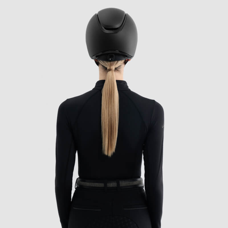Person wearing LeMieux Verv® Matte Black Competition Helmet, hair in a low ponytail.