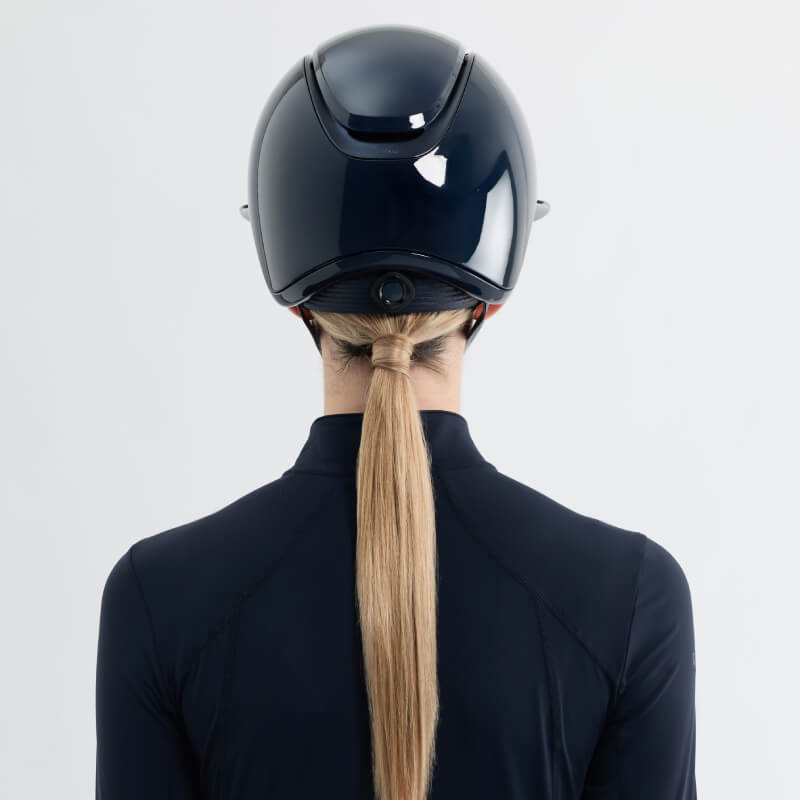 Rider with long blonde ponytail wearing LeMieux Verv® Competition Helmet Gloss Navy, seen from behind.