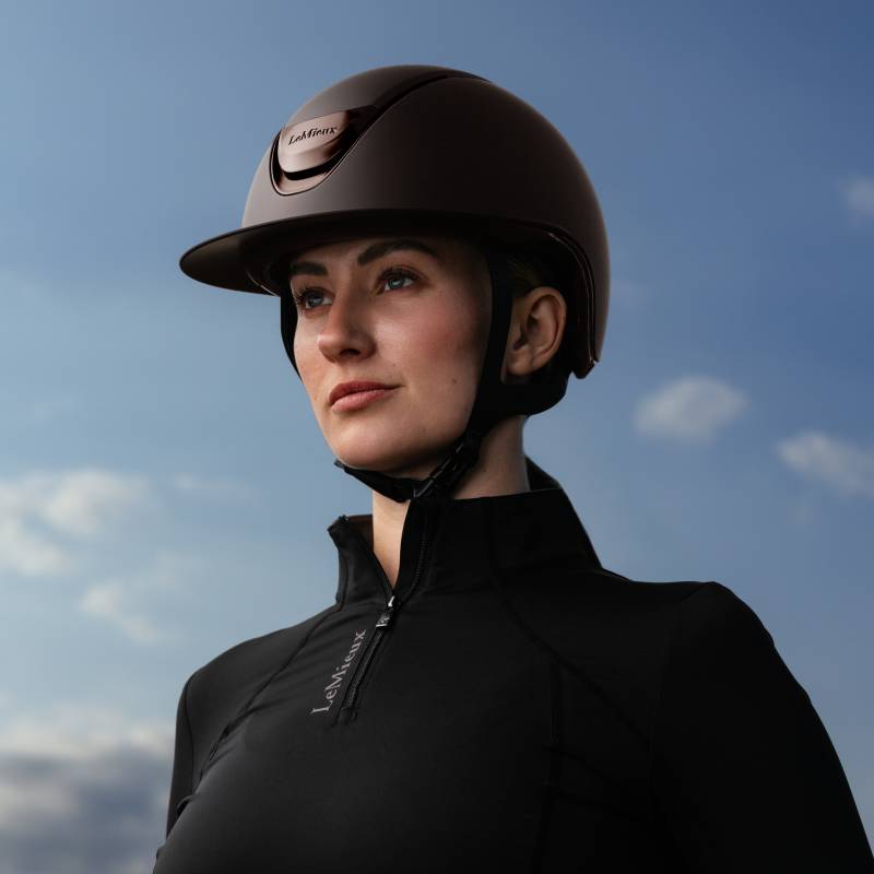 Person in a LeMieux Verv® Matte Brown Helmet and black jacket against a cloudy sky background.