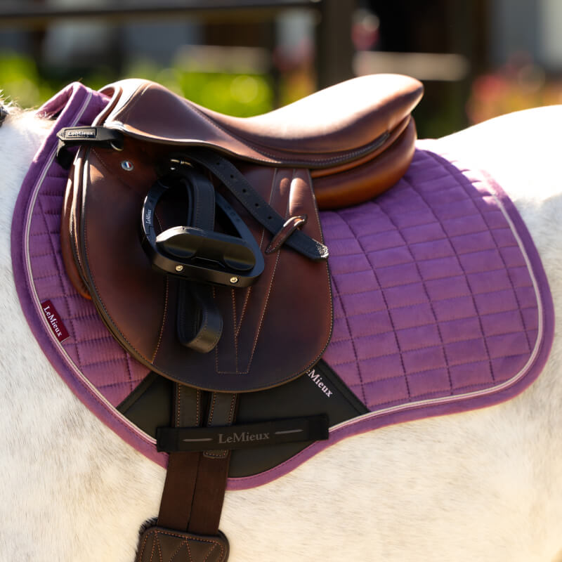 A brown saddle on a LeMieux Mini Suede Close Contact Square Mallow on a white horse.