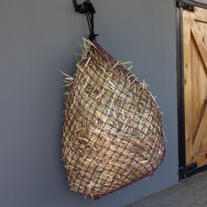 A LeMieux Hippo Lite Haynet Navy/Mallow filled with hay hangs on a gray wall.