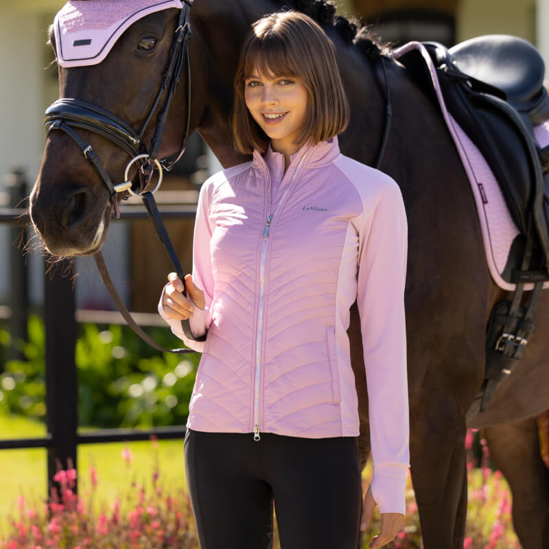Woman in LeMieux Juliette Jacket Fondant stands by a brown horse in pink gear.