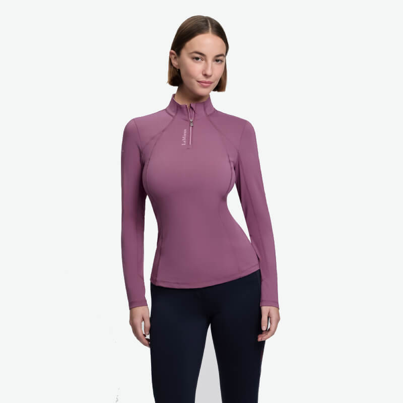 Woman in LeMieux Classique Baselayer Mallow and black pants stands against a white background.