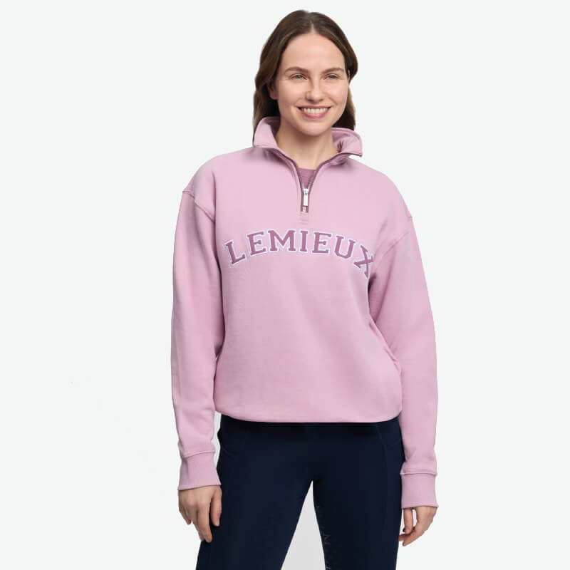 Smiling woman in pink LeMieux Kelsie Quarter Neck Sweat Fondant and dark pants, white background.