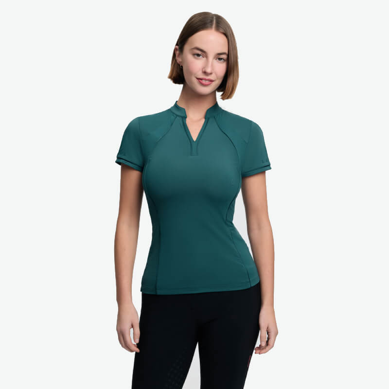 Woman in a LeMieux Lisa Mesh Baselayer Jungle and black pants stands against a plain background.