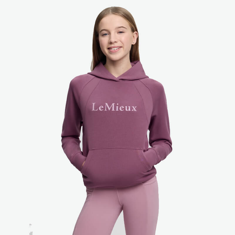 Smiling girl in LeMieux Young Rider Nancy Hoodie Mallow, hands in hoodie pocket.