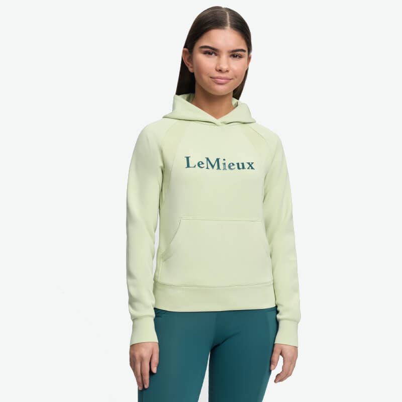 In a LeMieux Young Rider Nancy Hoodie Macaron and teal pants, against a white backdrop.