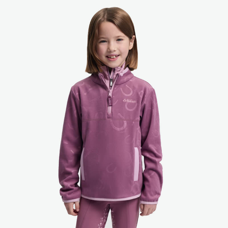 Smiling girl in a LeMieux Mini Maggie Fleece Mallow and pants stands against a white background.