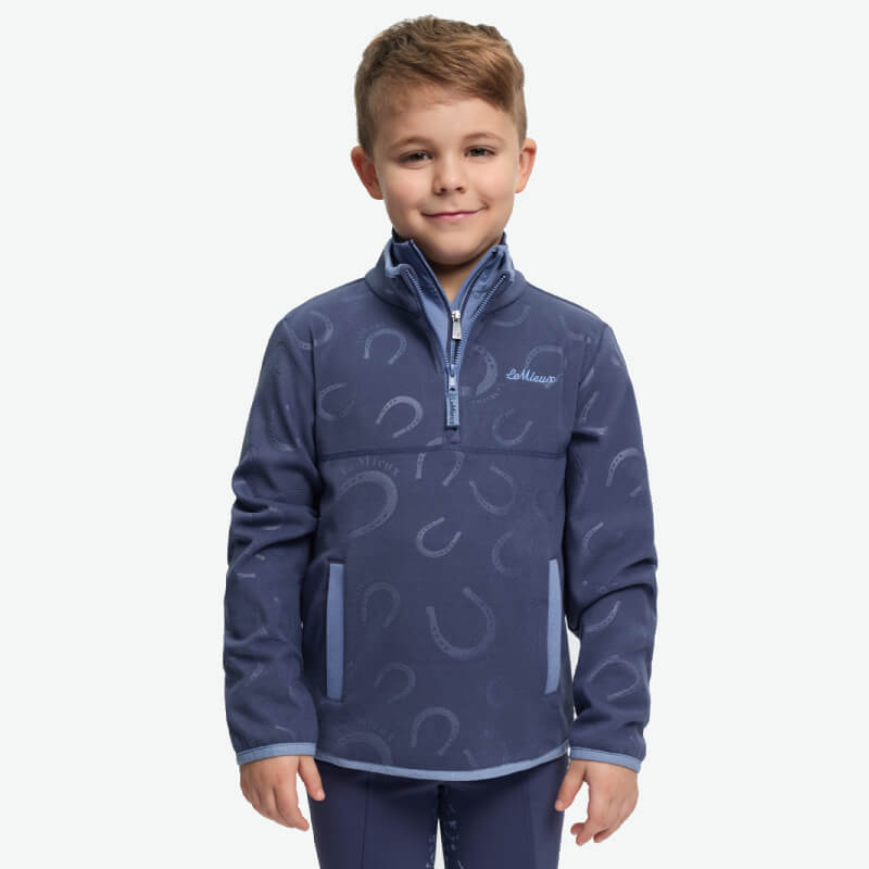 Smiling boy in LeMieux Mini Maggie Fleece Shadow with horseshoe pattern, on white background.
