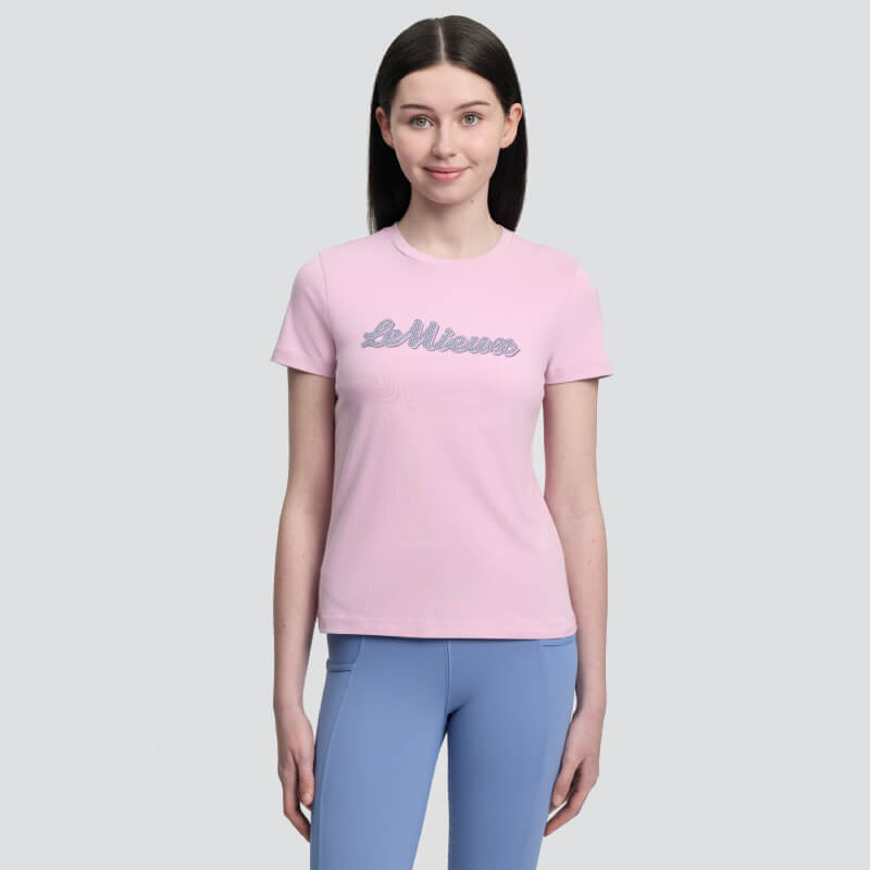 Woman wears LeMieux Young Rider Arianna T-Shirt Fondant and blue leggings against plain background.