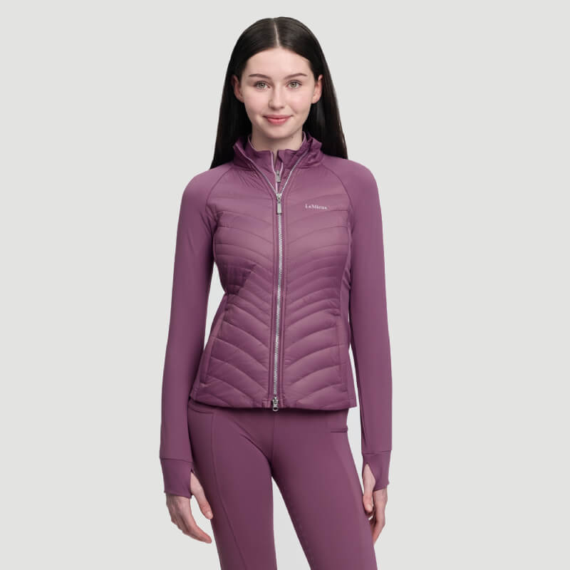 Woman in a LeMieux Young Rider Josephine Jacket Mallow stands against a plain light gray background.
