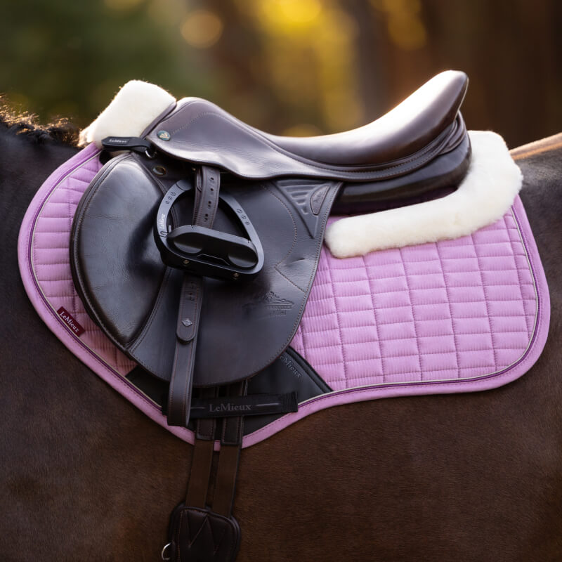 Close-up of a black saddle with a pink LeMieux Merino+ Suede Close Contact Square Fondant pad.