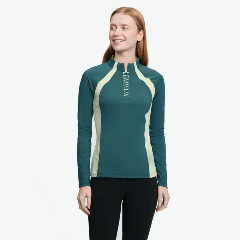 Woman smiling in a LeMieux Philippa Mesh Baselayer Jungle, teal and light yellow athletic top.