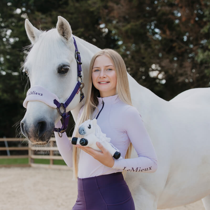 Young woman in light purple with a white horse and LeMieux Harlow Tiny Beanie Pony Panda.
