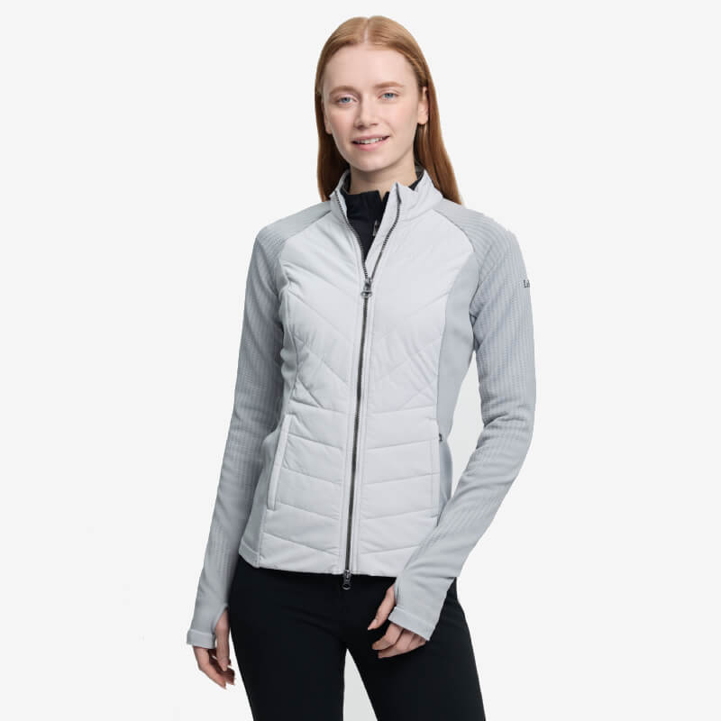 Woman in a LeMieux Maddie Jacket Grey and helmet sits on a horse with a scenic backdrop.