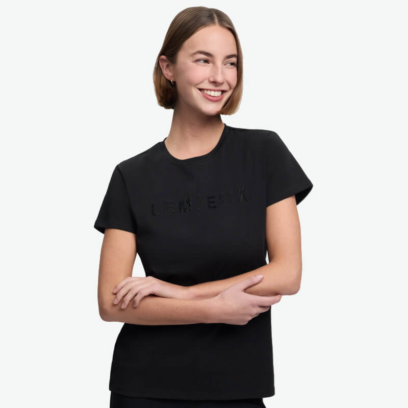 Smiling woman in a LeMieux Brilliance T-Shirt Black, arms crossed, on a white background.