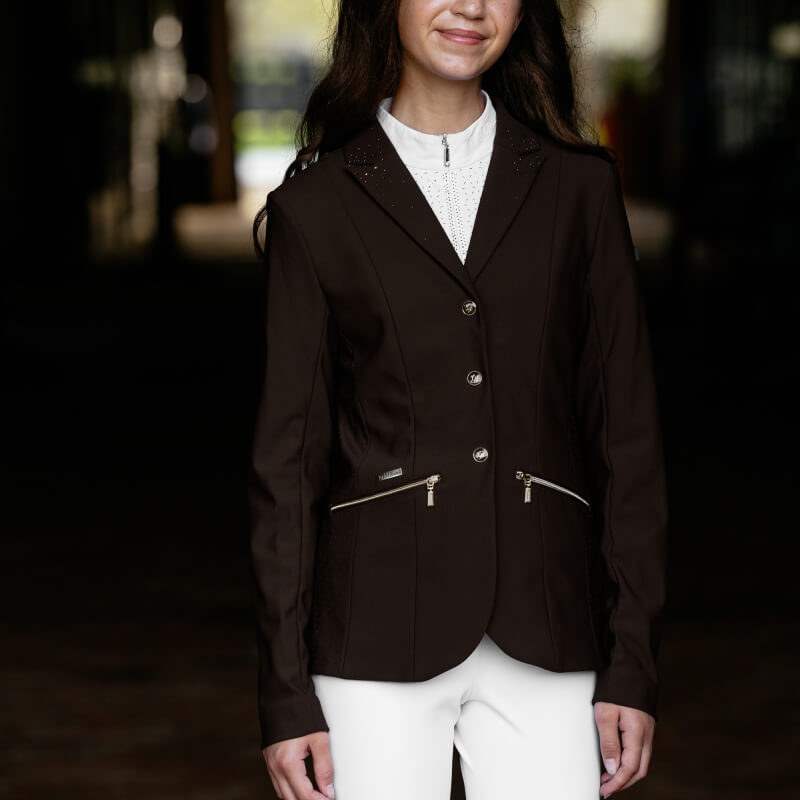 Young rider wears a LeMieux Brilliance Junior Pro Show Jacket in Espresso and white pants indoors.