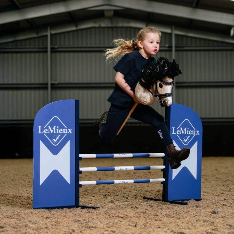 A girl plays indoors, jumping the LeMieux Hobby Horse Benetton Blue over a show jump.