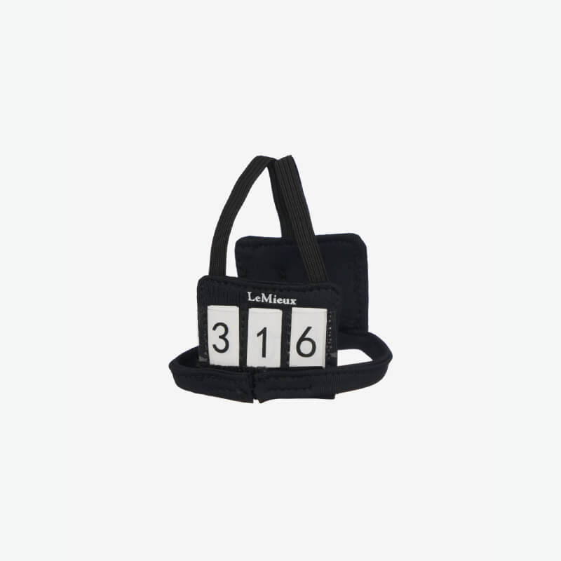 LeMieux Toy Rider in black body protector & number bib sits on an orange pole outdoors.