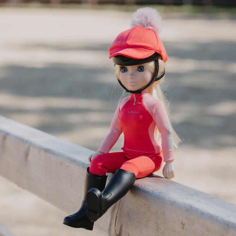 LeMieux Harlow Toy Rider Coral Crush doll sits on a wooden fence outdoors.