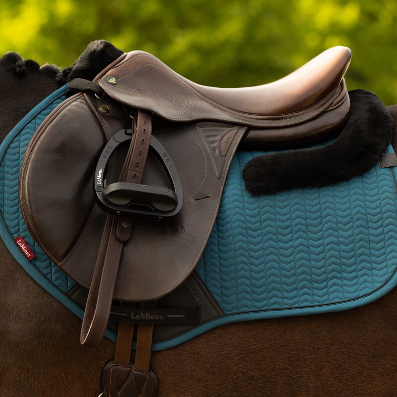 Brown leather saddle on LeMieux Merino+ Essence Close Contact Square Jungle with green foliage.