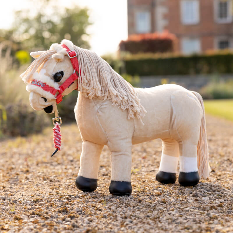 A plush toy horse wears the LeMieux Harlow Toy Pony Headcollar &amp; Leadrope Coral Crush.