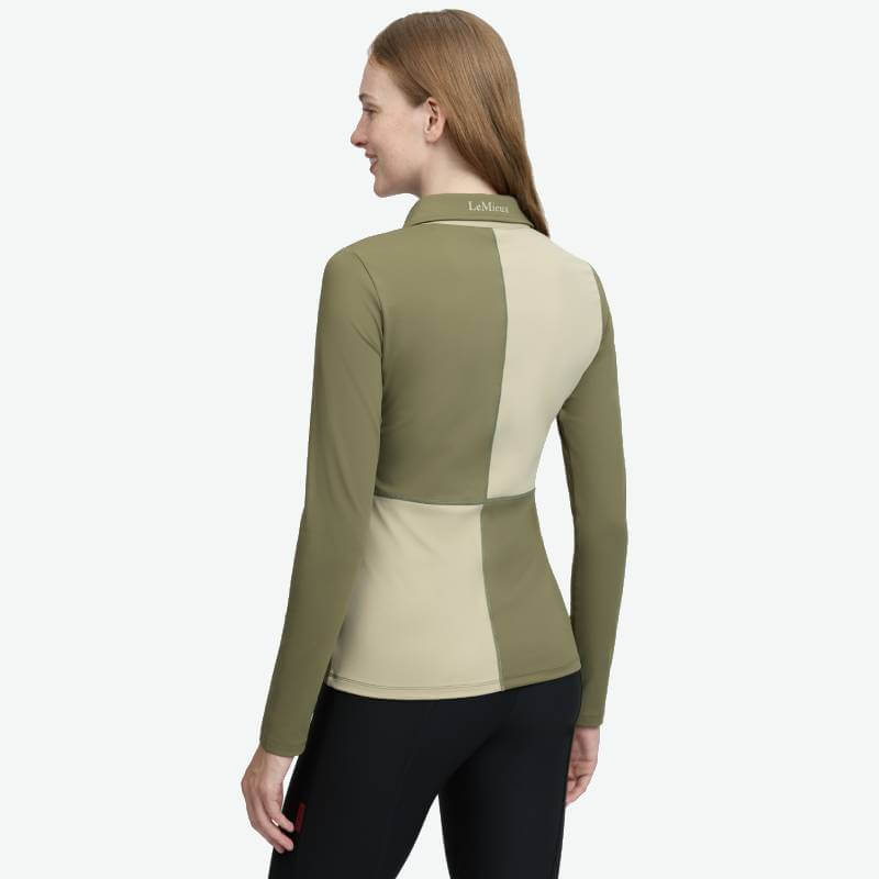 Woman in LeMieux Harlequin Rugby Shirt Baselayer Willow/Pear, seen from the back, smiling.