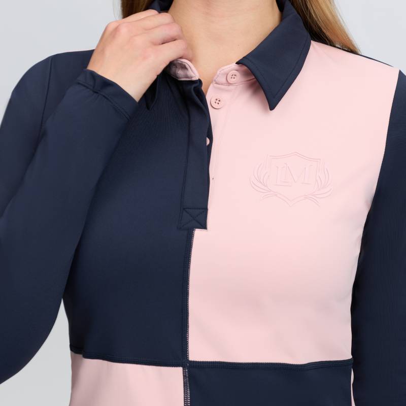 Wearing a LeMieux Harlequin Rugby Shirt Baselayer Petal/Navy, the person touches their collar.