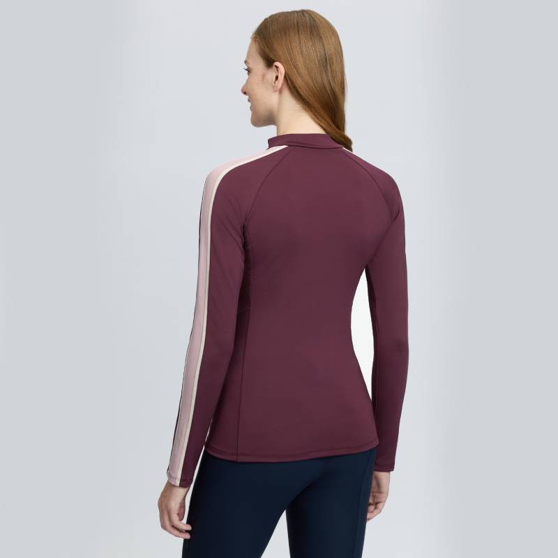 A woman wears a LeMieux Talia Turtle Neck Baselayer Bramble, standing with her back facing us.