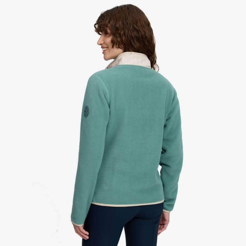 Woman in LeMieux Piper Popper Fleece Aloe, facing away, with short brown curls and dark pants.