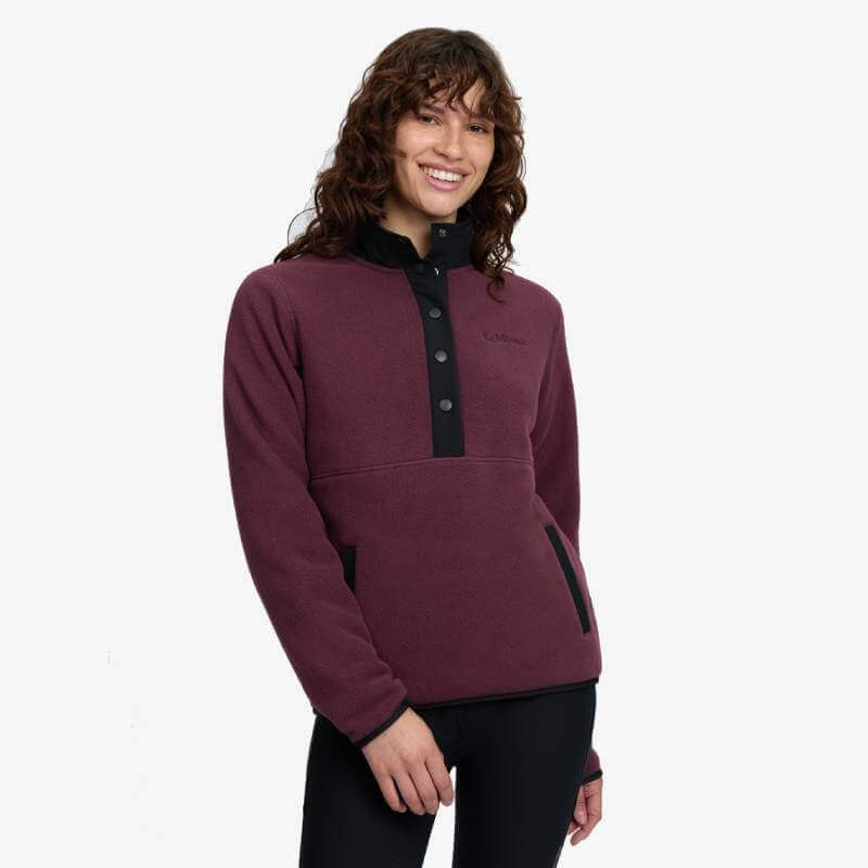 Smiling in a LeMieux Piper Popper Fleece Bramble with black trim, on a white backdrop.