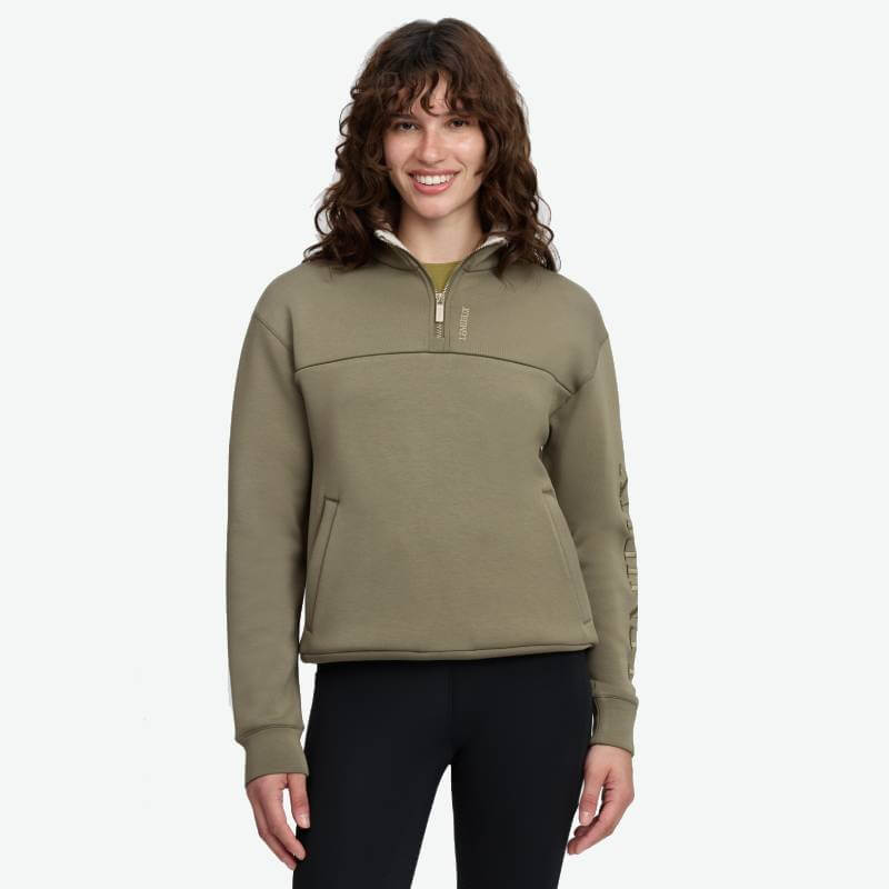 Woman smiles in LeMieux Scarlet Quarter Zip Sweat Willow Green, standing by a white background.