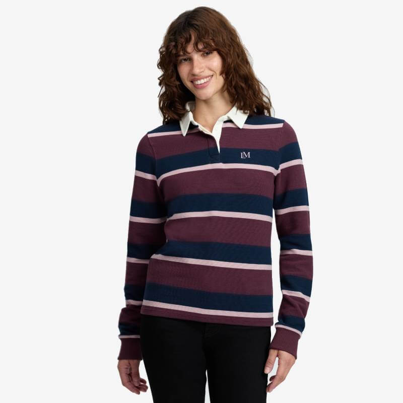 Woman in LeMieux Sloane Stripe Rugby Shirt Bramble and black pants smiles at the camera.